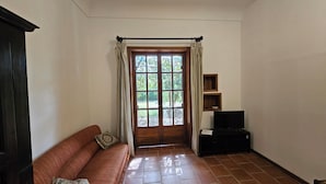 A room with a wooden door, a brown sofa, a television on a stand, and a tiled floor. - La Pineta (Lecce)