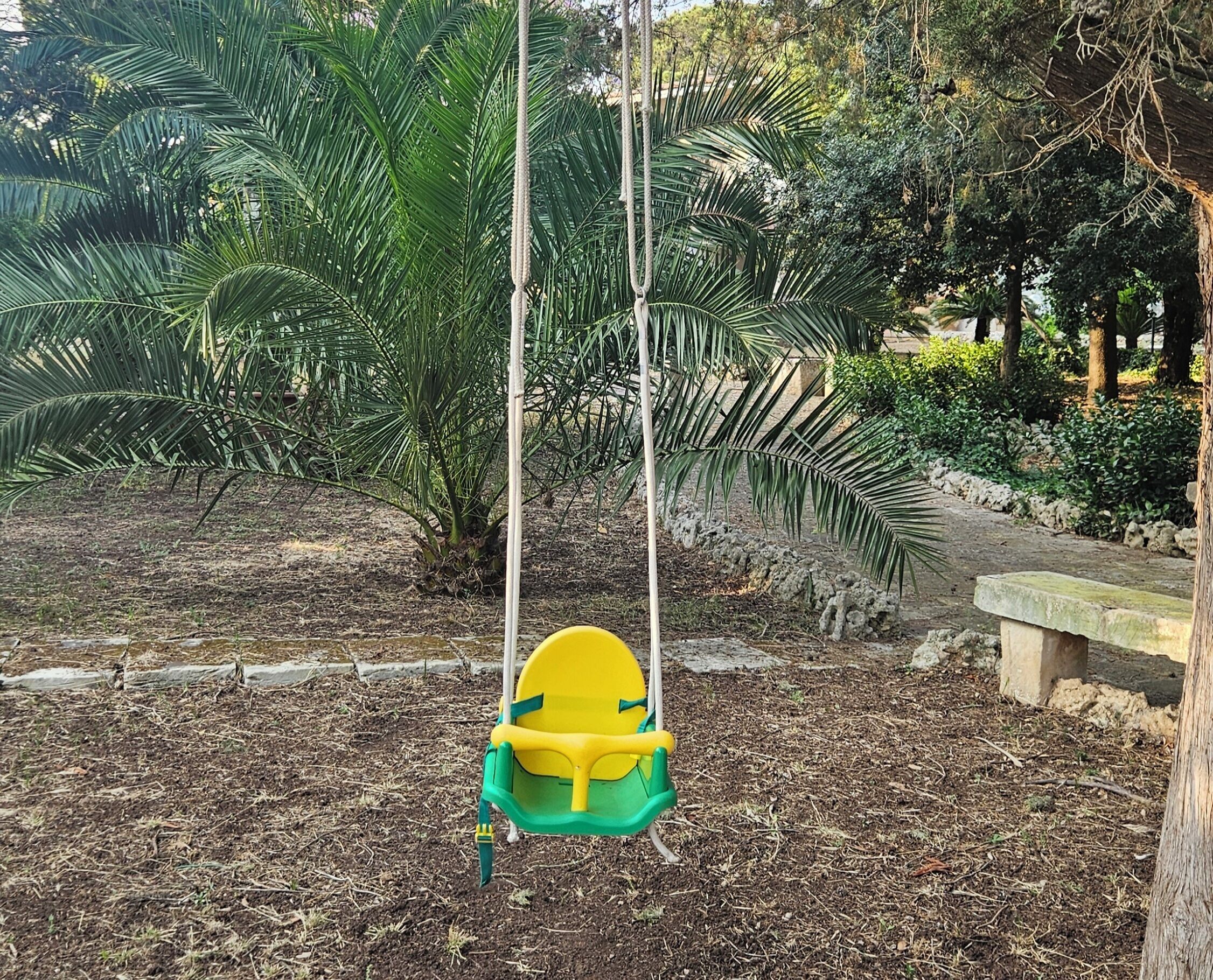 Un columpio en un jardín con palmeras y un banco de piedra.