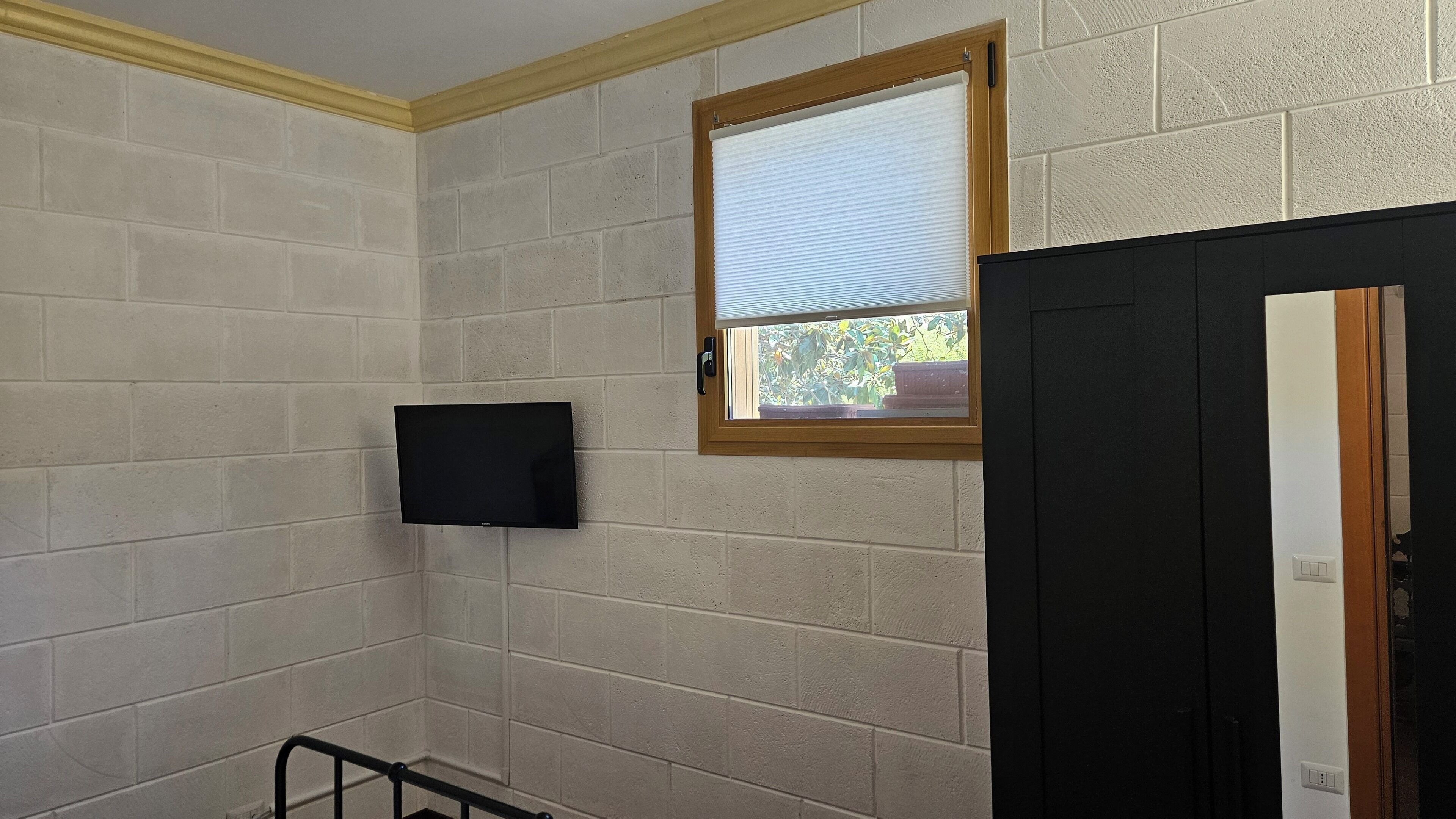 A bathroom with a tiled wall, a mounted TV, and a window with a view of greenery.