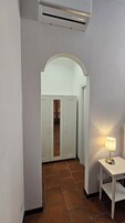 Un pasillo con una puerta blanca, una mesita con lámpara y un equipo de aire acondicionado en la pared.