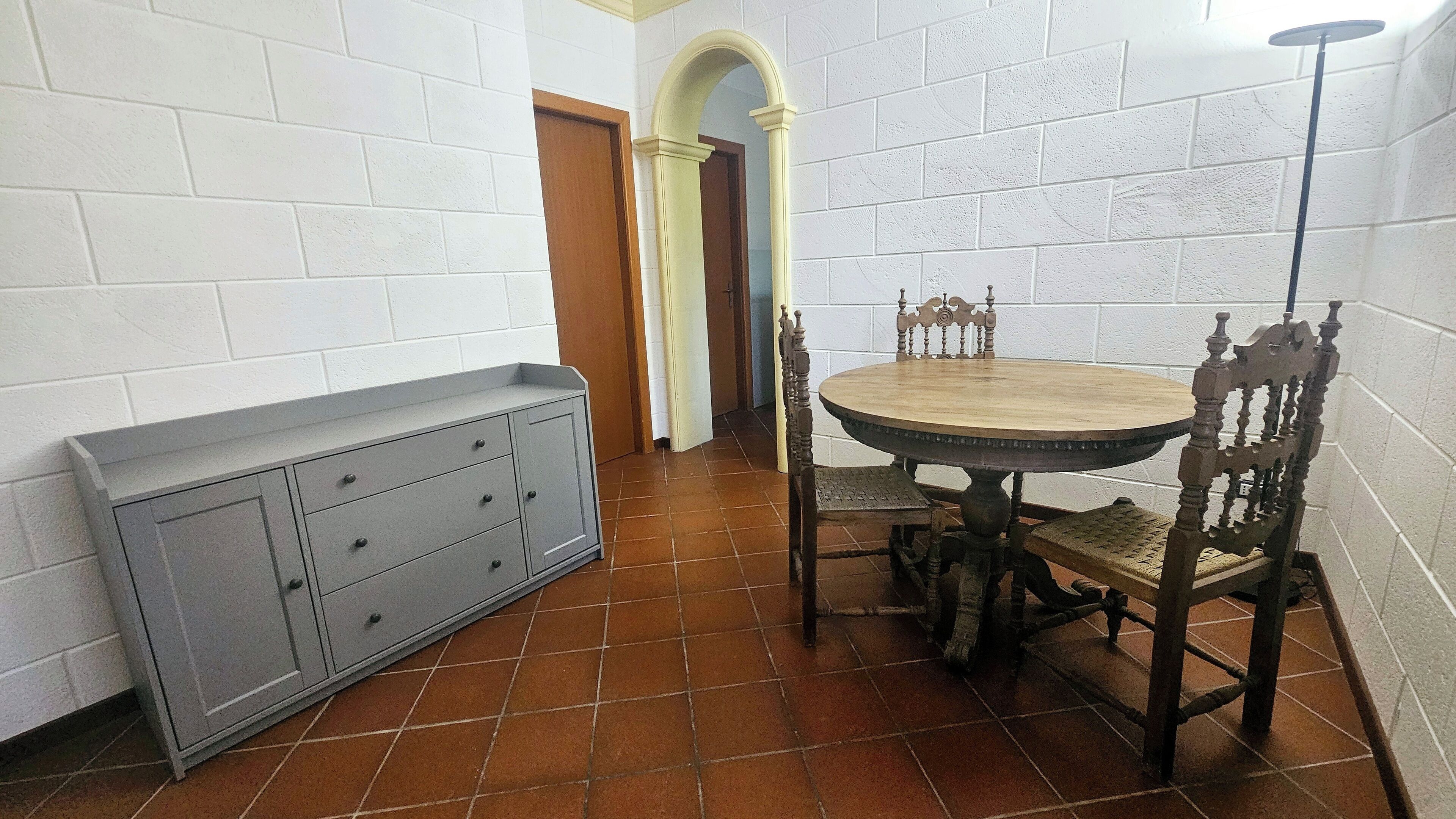 A dining area with a round wooden table, two chairs, a bench, and a cabinet.