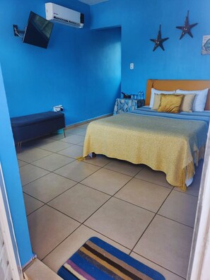 Una habitación con una cama, un banco y un televisor montado en la pared.