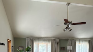 A spacious dining area with a large wooden table and chairs, a ceiling fan, and a view of the outdoors through large windows with curtains. - Charming 3-bedroom house in tranquil Cloudcroft with WiFi (Cloudcroft)