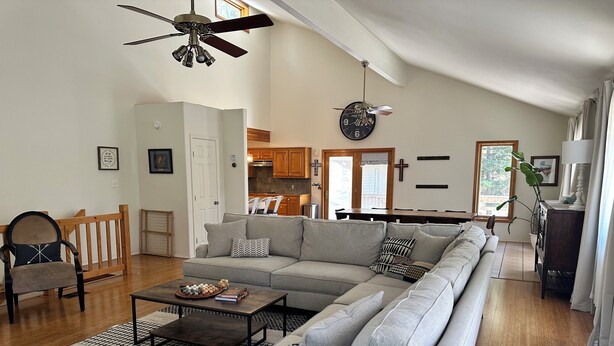 A spacious living room with a large grey sectional sofa, a coffee table, and a wooden chair. A ceiling fan and a clock are visible. - Charming 3-bedroom house in tranquil Cloudcroft with WiFi (Cloudcroft)