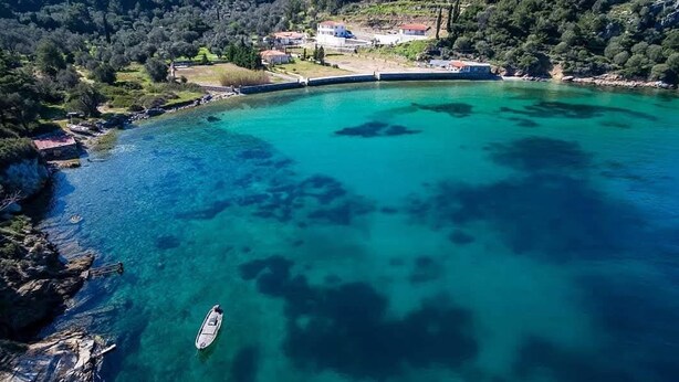 A coastal area with clear turquoise waters, a boat, and a building complex on a hillside. - Serenity Villa (Charavgi)