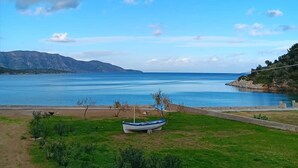 A coastal landscape with a boat on a grassy area near the water, a clear sky, and distant mountains. - Serenity Villa (Charavgi)