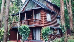 A log cabin with a balcony, surrounded by trees.