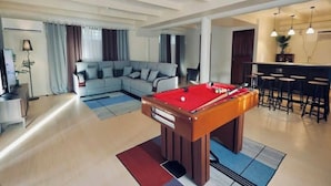 A modern living room with a pool table, a sofa, and a bar area.
