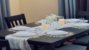 A dining table set for four with white plates, clear glasses, and candles.