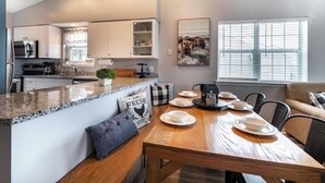 A modern kitchen with white cabinets, a granite countertop, and a dining area with a wooden table set for four.