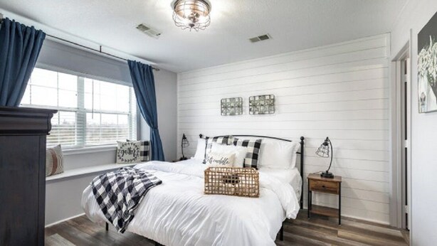A bedroom with a bed, a window with curtains, a bedside table, and wall decor.