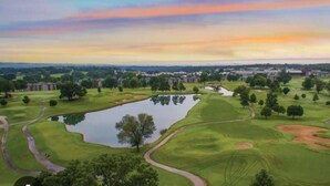 A golf course with a pond, trees, and buildings in the background.