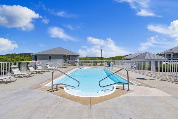 A swimming pool with lounge chairs and a fenced area, surrounded by buildings with grey roofs.