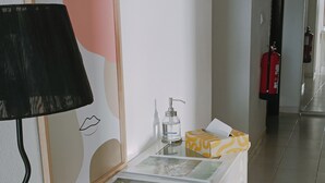 Un pasillo con una mesa blanca que exhibe fotografías enmarcadas, una lámpara negra, un dispensador de gel antibacterial y un extintor.