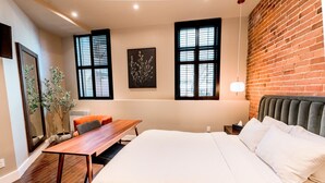 Ein modernes Hotelzimmer mit einem großen Bett, einem Holztisch, zwei Stühlen, einer Topfpflanze und einer Ziegelwand.