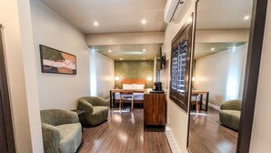 Een hotelkamer met een bed, een bureau, twee fauteuils, een spiegel en een lijst met een foto aan de muur.