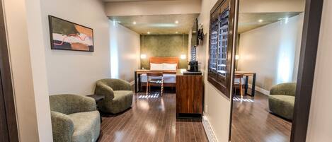 Une chambre d’hôtel avec un lit, un bureau, deux fauteuils, un miroir et un tableau encadré au mur.