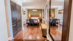 Habitación de hotel con suelo de madera, cama con cabecera de madera, dos mesitas de noche con lámparas, un banco y un espejo grande.