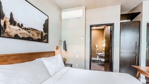 Habitación de hotel con una cama grande, un cuadro en la pared, un equipo de aire acondicionado, un escritorio y un armario.