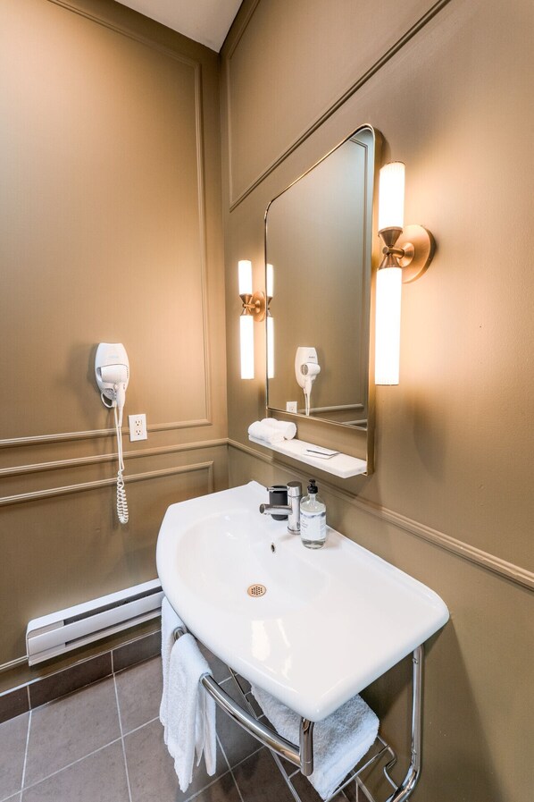 Un baño de hotel con un lavabo blanco, un espejo, un secador de pelo y un perchero para toallas.