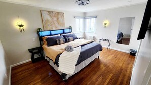 Quarto com uma cama grande, janela, ventilador de teto e luminárias fixadas na parede.