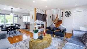 Uma sala de estar moderna com área de jantar, uma escada e um relógio grande na parede.