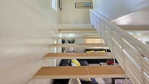 A modern staircase with wooden steps and white railings, leading to a living area with a sofa and cushions.