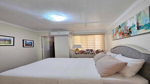 A neatly made bed with a headboard, a bedside table with a lamp, and a wall with framed pictures.