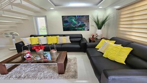A modern living room with a sectional sofa, a coffee table with decorative items, a large abstract painting, and a staircase.