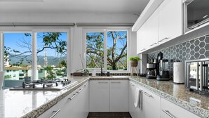 A modern kitchen with white cabinets, granite countertops, and a view of mountains and buildings through large windows. - Cozy 2BR in Versalles – Walk to Beach & Dining (Puerto Vallarta)