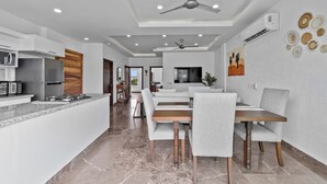 A modern kitchen with a built-in oven and microwave, a dining area with a wooden table and grey upholstered chairs, and a ceiling fan. - Cozy 2BR in Versalles – Walk to Beach & Dining (Puerto Vallarta)