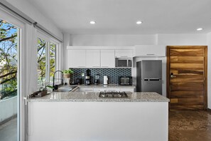 Cozinha moderna com armários brancos, bancada de granito, micro-ondas embutido e porta de madeira.
