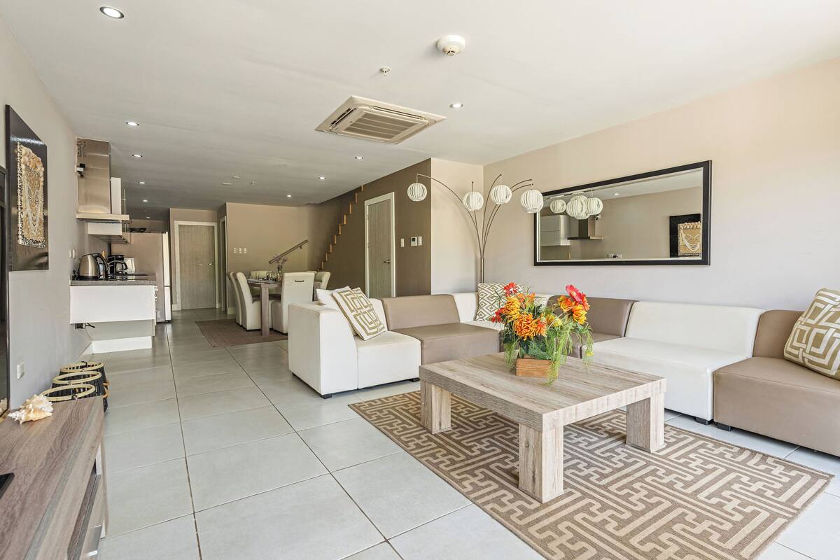 A modern living room with a sofa, coffee table, and a dining area.