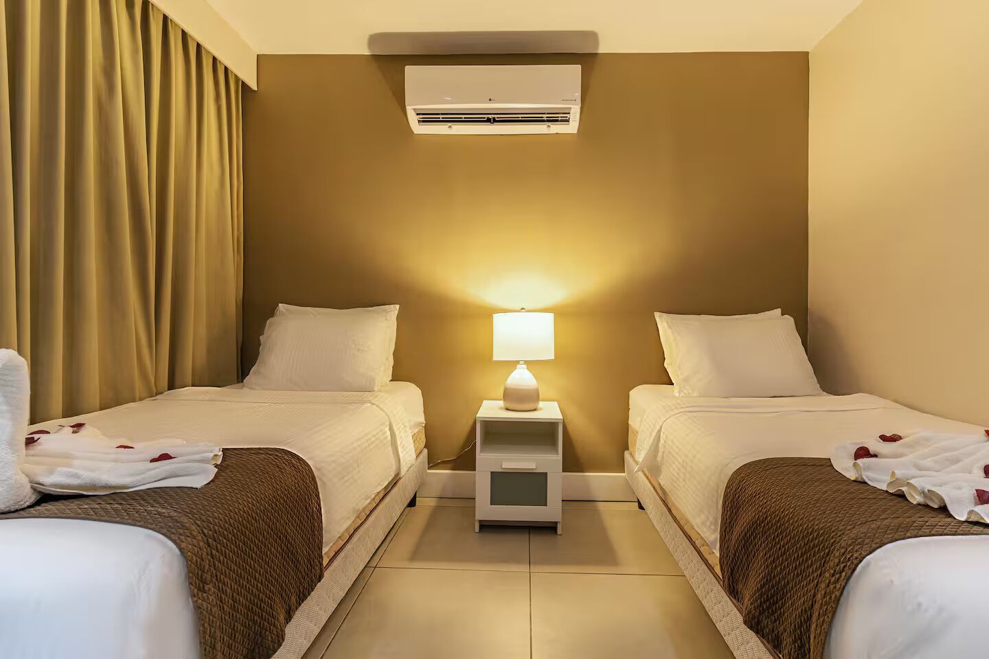 Une chambre d’hôtel avec deux lits, une table de chevet avec une lampe, un climatiseur et un rideau.