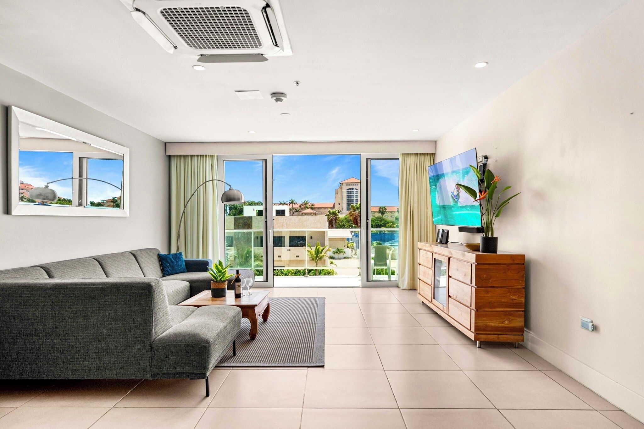 A modern living room with a grey sofa, a wooden cabinet, and a large TV screen.