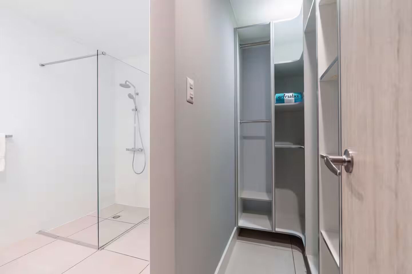 A bathroom with a glass shower enclosure and a walk-in closet with shelves.