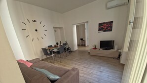 A modern living room with a brown sofa, a dining area with a glass table, and a TV on a wooden cabinet. - Central and quiet apartment, 1 min from the Duomo and 3 min from Lake Como. (Como)