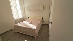 A bedroom with a bed, a bedside table, a wall-mounted air conditioner, and a window with sheer curtains. - Central and quiet apartment, 1 min from the Duomo and 3 min from Lake Como. (Como)