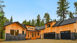 A modern wooden cabin with a central porch, multiple garage doors, and a gravel driveway. - Picturesque Cedar Retreat w/ Hot Tub (McCall)