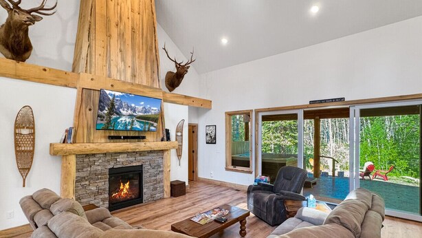 A spacious living room with a stone fireplace, leather sofas, and a large TV. - Picturesque Cedar Retreat w/ Hot Tub (McCall)