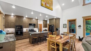 A spacious kitchen with wooden cabinets, a central island with stools, and a dining area with a wooden table and chairs. - Picturesque Cedar Retreat w/ Hot Tub (McCall)