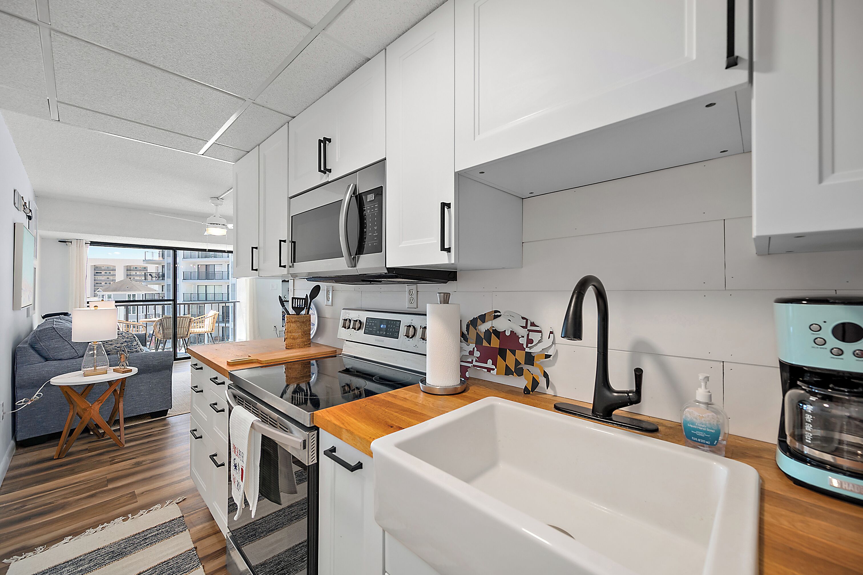 Una cocina moderna con armarios blancos, encimera de madera, microondas de acero inoxidable, cafetera y un lavabo grande.