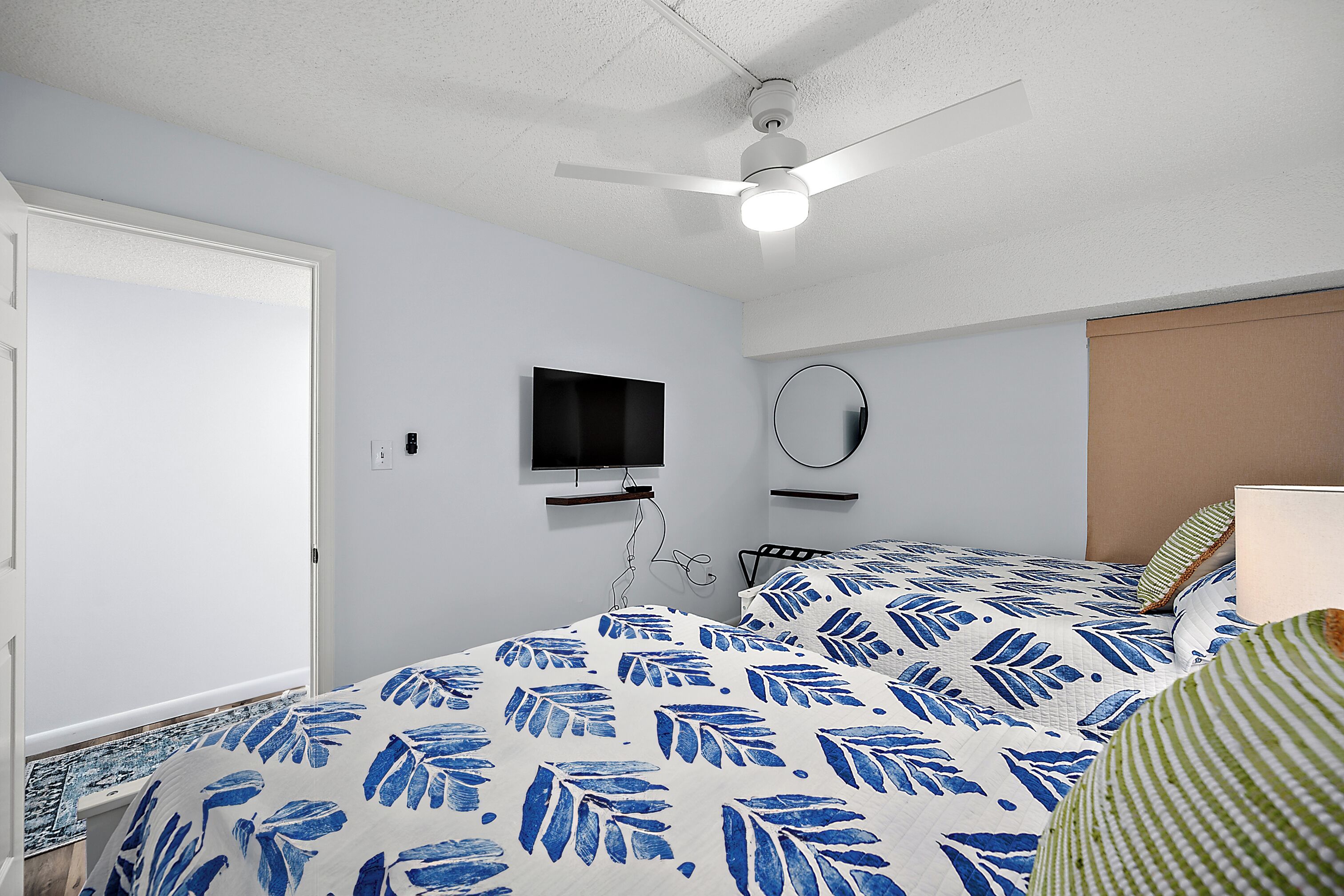 A bedroom with a bed, a ceiling fan, a TV, and a mirror.