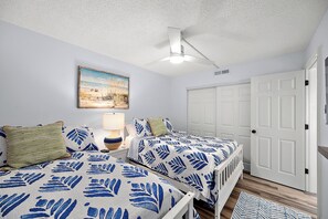 A bedroom with two beds, a ceiling fan, a painting, and a white door. - Ocean Block 1 Bedroom-Sleeps6-Pool (Ocean City)
