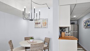 A dining area with wicker chairs, a white table, and a modern chandelier.