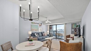 A modern living room with a grey sofa, wicker chairs, a dining table, and a chandelier.