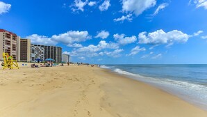 A beach with a hotel in the background, sandy shore, and clear blue sky. - Oceanfront 2 Bed/2Bath,IndoorPool,Game Room (Ocean City)