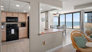 A modern kitchen with a built-in microwave, oven, and coffee maker, a dining area with a view of the beach, and a cozy seating area with a view. - Oceanfront 2 Bed/2Bath,IndoorPool,Game Room (Ocean City)