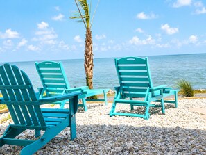 Three turquoise Adirondack chairs facing a beach with a palm tree and ocean view. - Dancing Dolphin-Waterfront! Hot Tub, Pool, Arcade. NEW! Golf Cart avail for 2027 (Fulton)