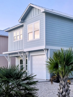 A two-story house with a garage, a covered porch, and a gravel driveway.